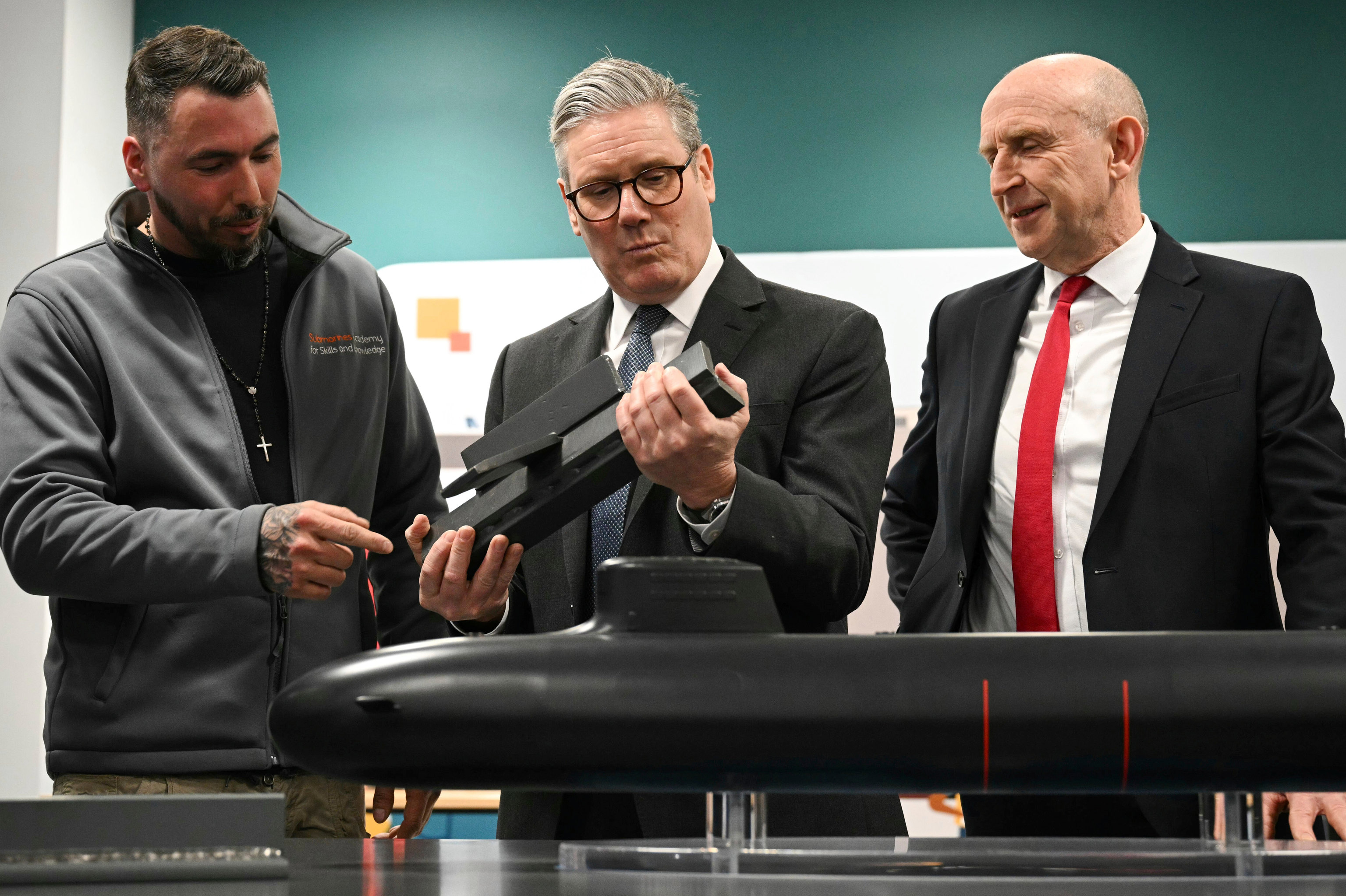 Britain's Prime Minister Keir Starmer, center, and Defence Secretary John Healey, right, meet with BAE system apprentices as they look at a submarine model.