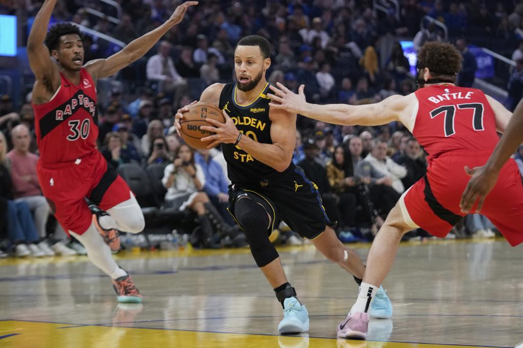 Golden State Warriors guard Stephen Curry, center, moves the ball between Toronto Raptors guard Ochai Agbaji (30)