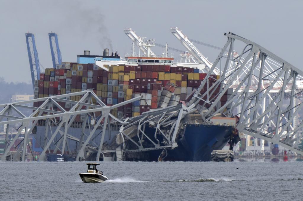 A boat moves past a container ship as it rests against wreckage of the Francis Scott Key Bridge