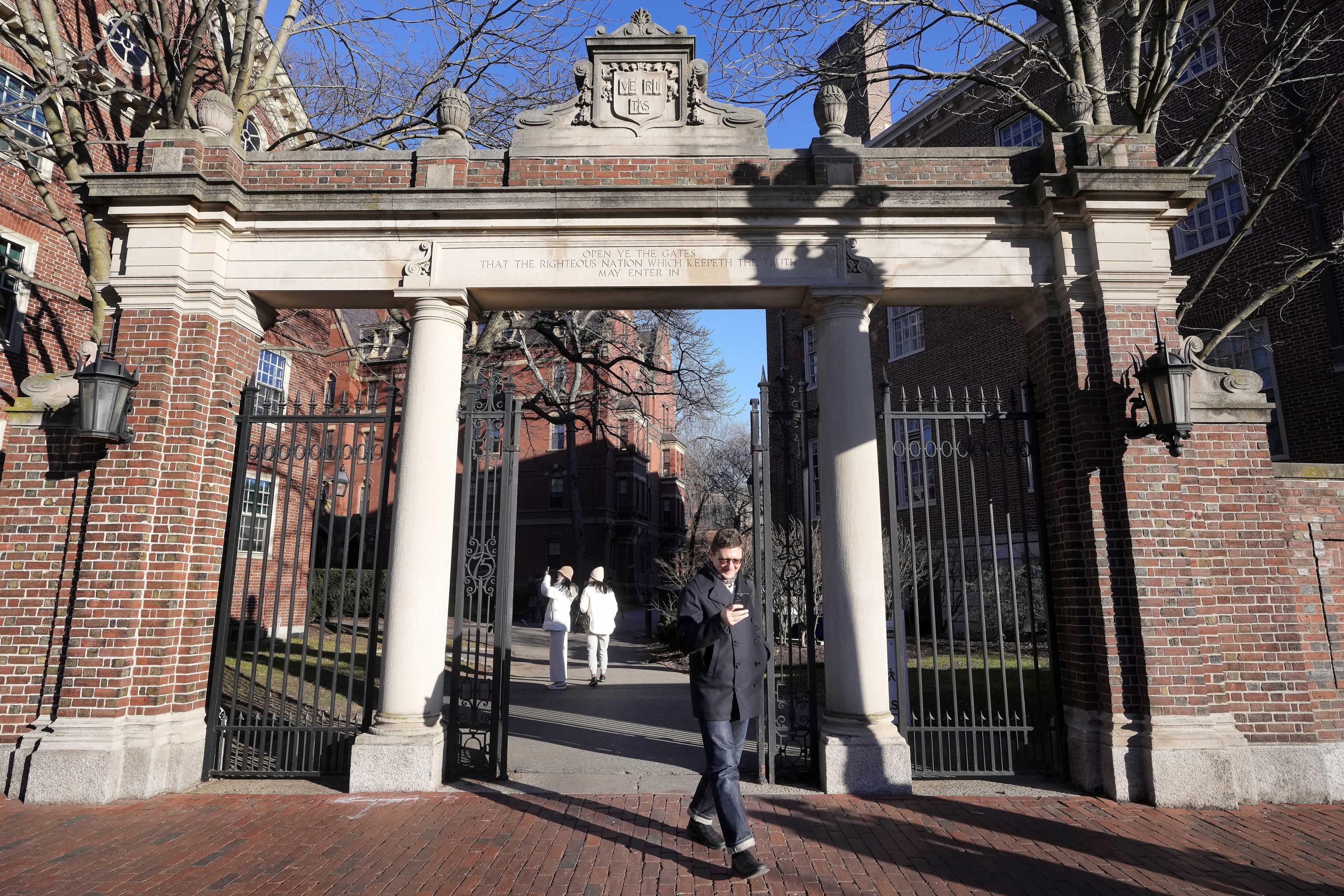 A passer-by walks through a gate to the Harvard University campus.