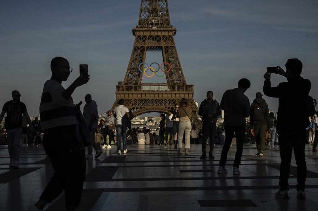 People use their smartphones near the Olympic rings that are displayed on the Eiffel Tower in Paris