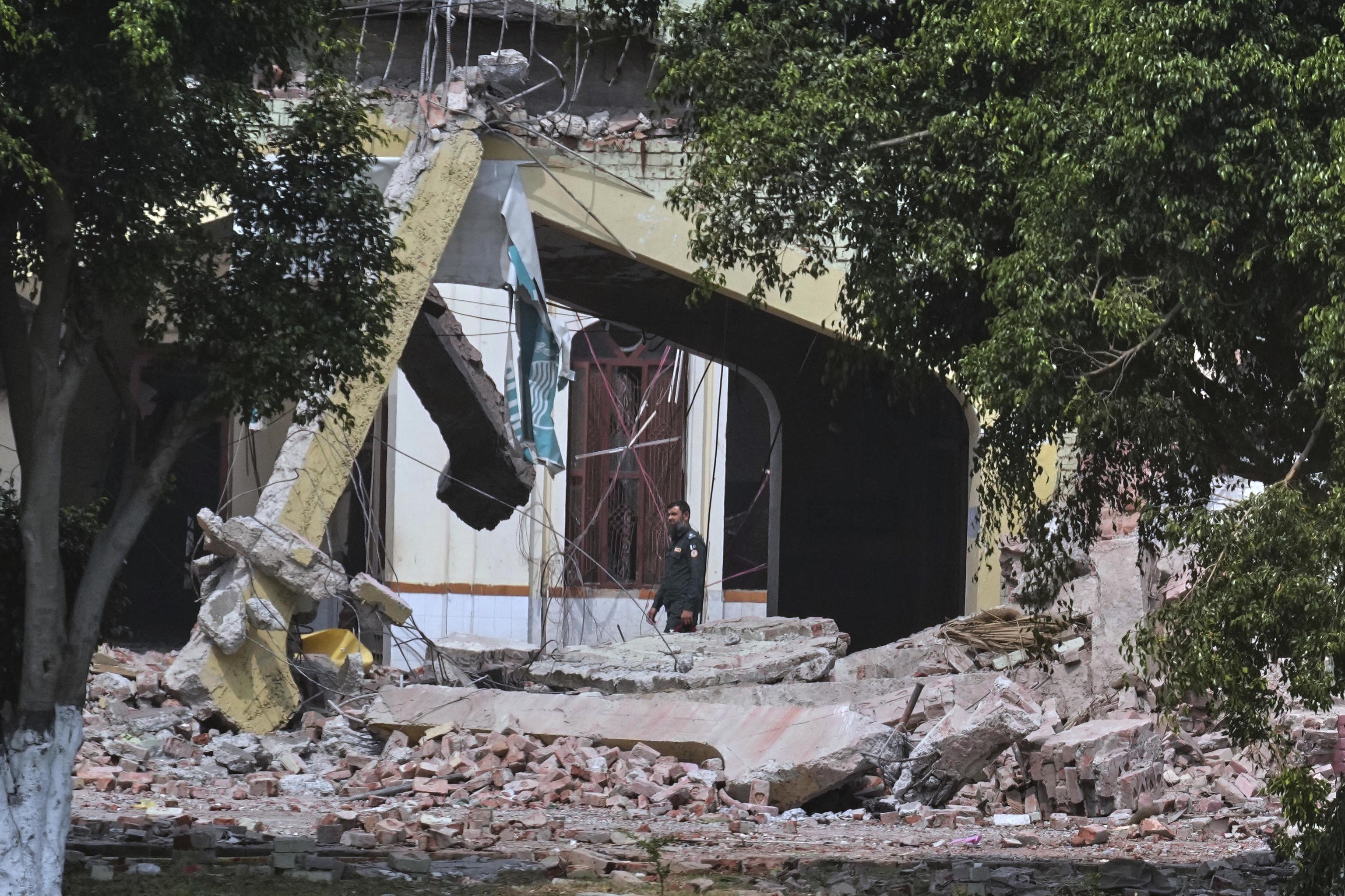A private security guard walks through rubble of a damaged building.