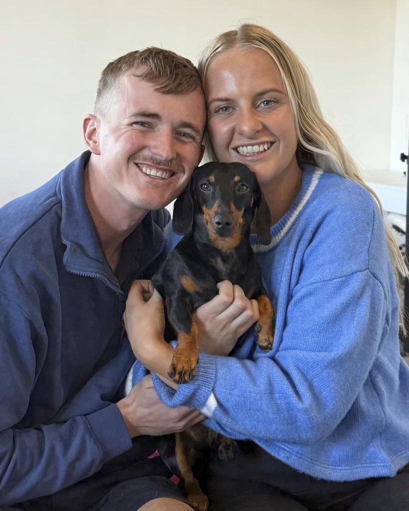 Georgia Gardner and her partner, Josh Fishlock, pose holding Valerie, their dachshund, after meeting on Kangaroo Island, South Australia.