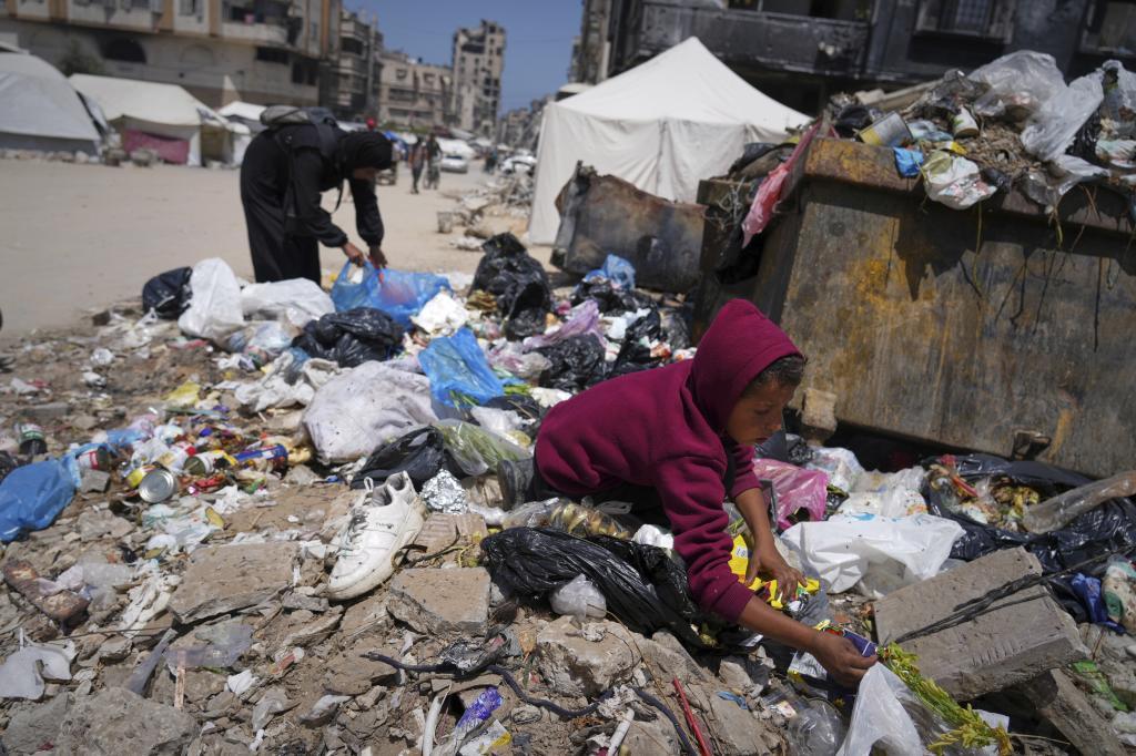 Islam Abu Taeima, a 40-year-old mother of five, left, and a boy look for some food on a pile of garbage in Gaza City