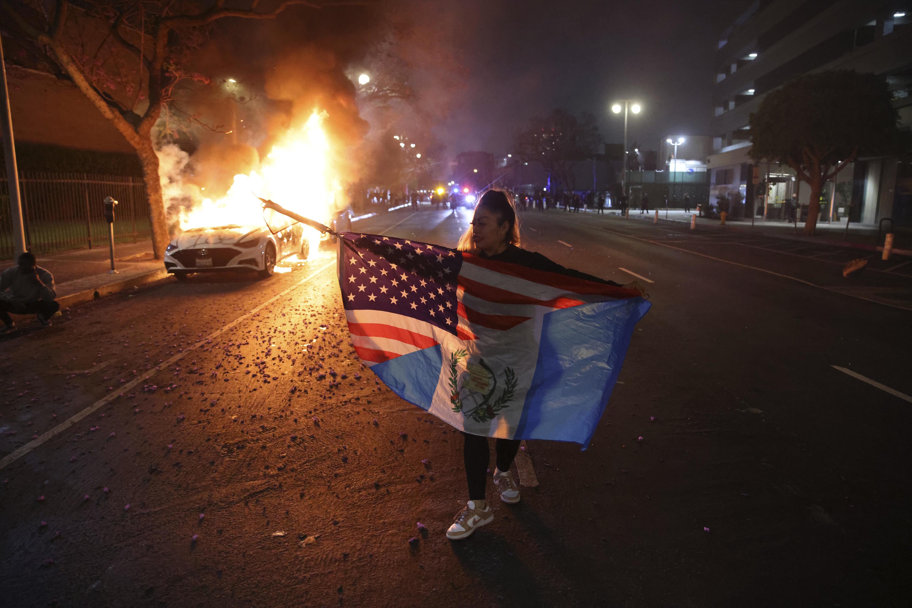 A protestor walks past a burning car during protests.