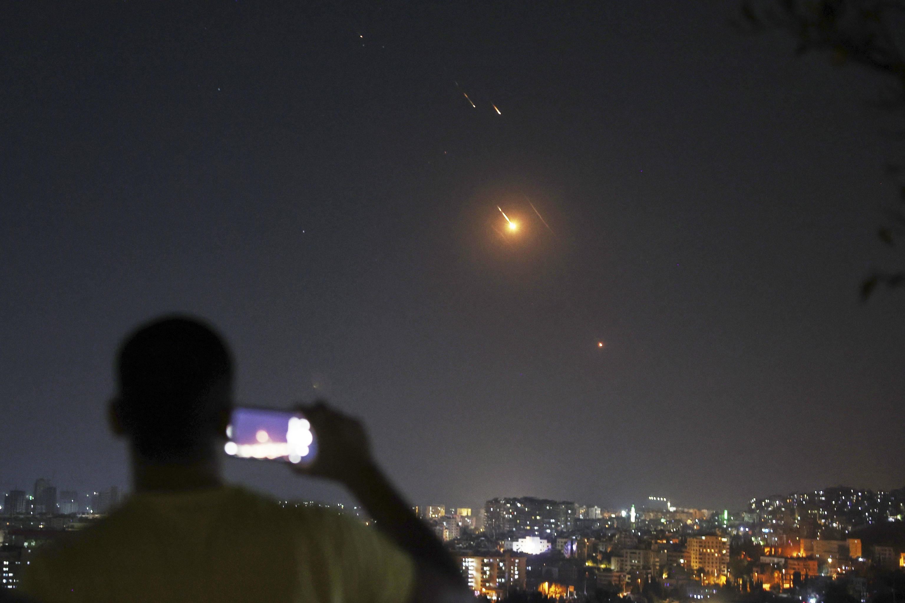 A man takes a photo with his mobile phone as missiles fired from Iran toward Israel fly over Damascus, Syria.