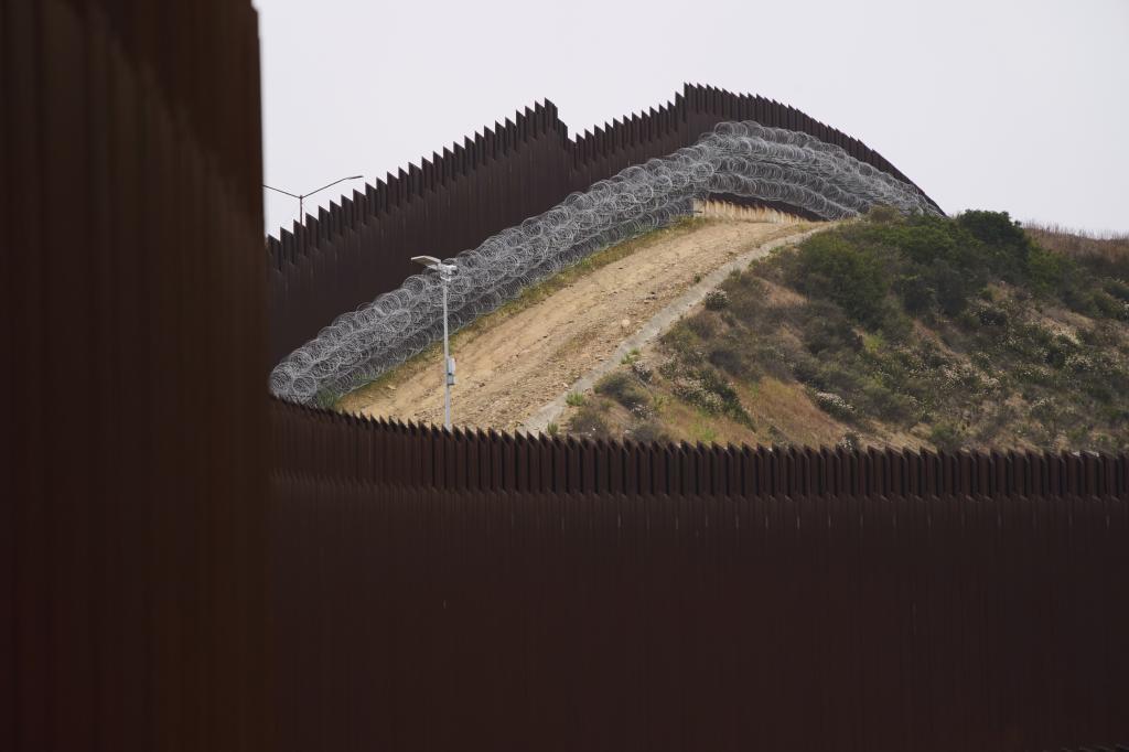 Concertina wire lines the interior of a border wall,