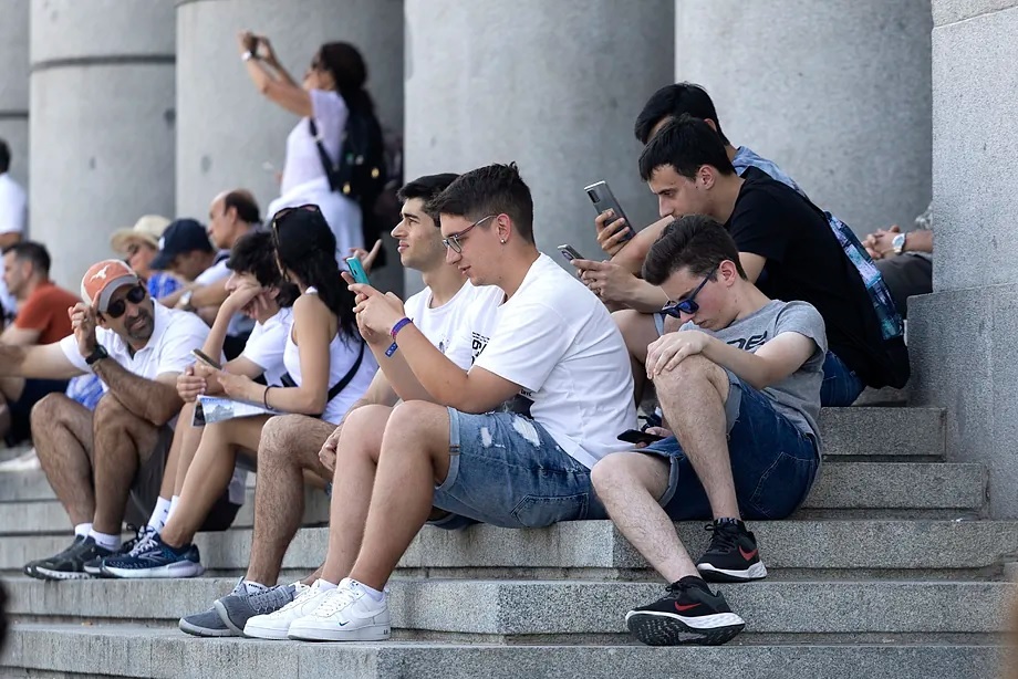 Young people with their phones on the stairs of the Royal Palace in Madrid.