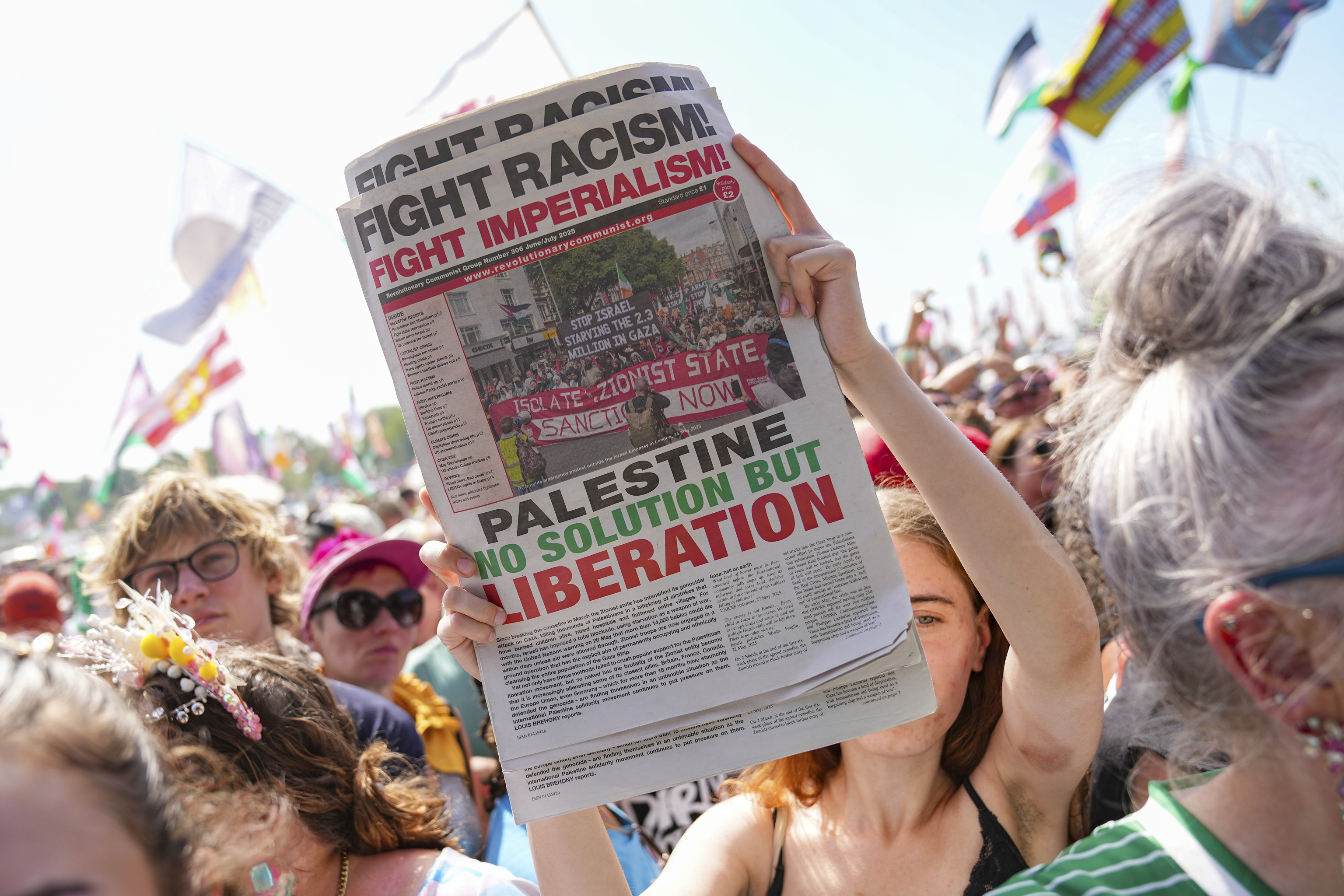 A festivalgoer holds a newspaper that reads "Fight Racism! Fight Imperialism! Palestine No Solution But Liberation" during the performance of hip hop trio Kneecap at Glastonbury Festival.