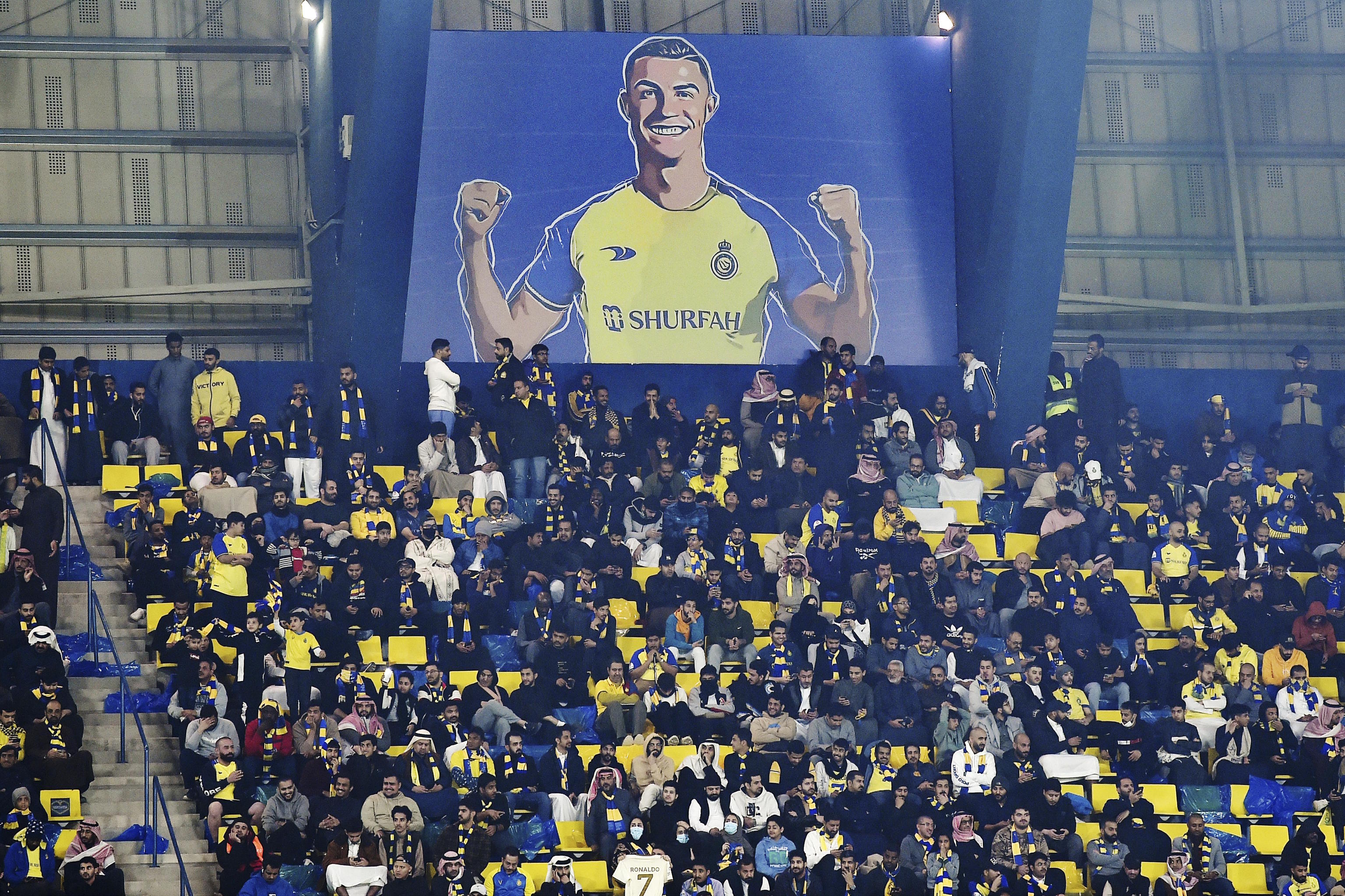 Al Nassr fans sit under a giant billboard of Cristiano Ronaldo.