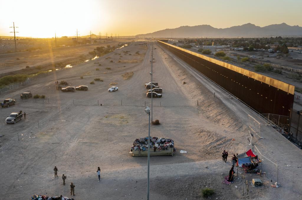 A small group of migrants, bottom right, are pictured while camping outside a gate in the border fence in El Paso, Texas