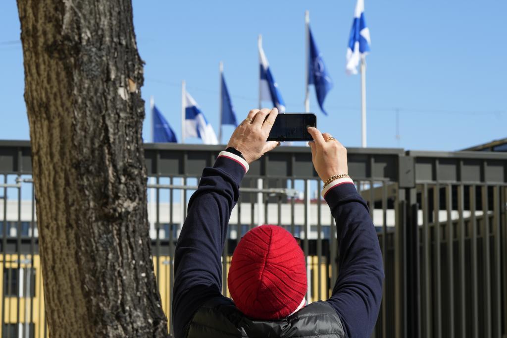 A man takes pictures as NATO and Finland flags flutter over the building of Ministry of Foreign Affairs in Helsinki