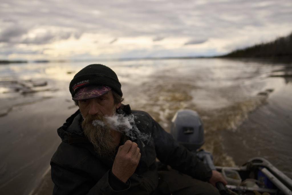 Jake Pogrebinsky smokes a cigarette while diving his boat on the Yukon River looking for logs to collect