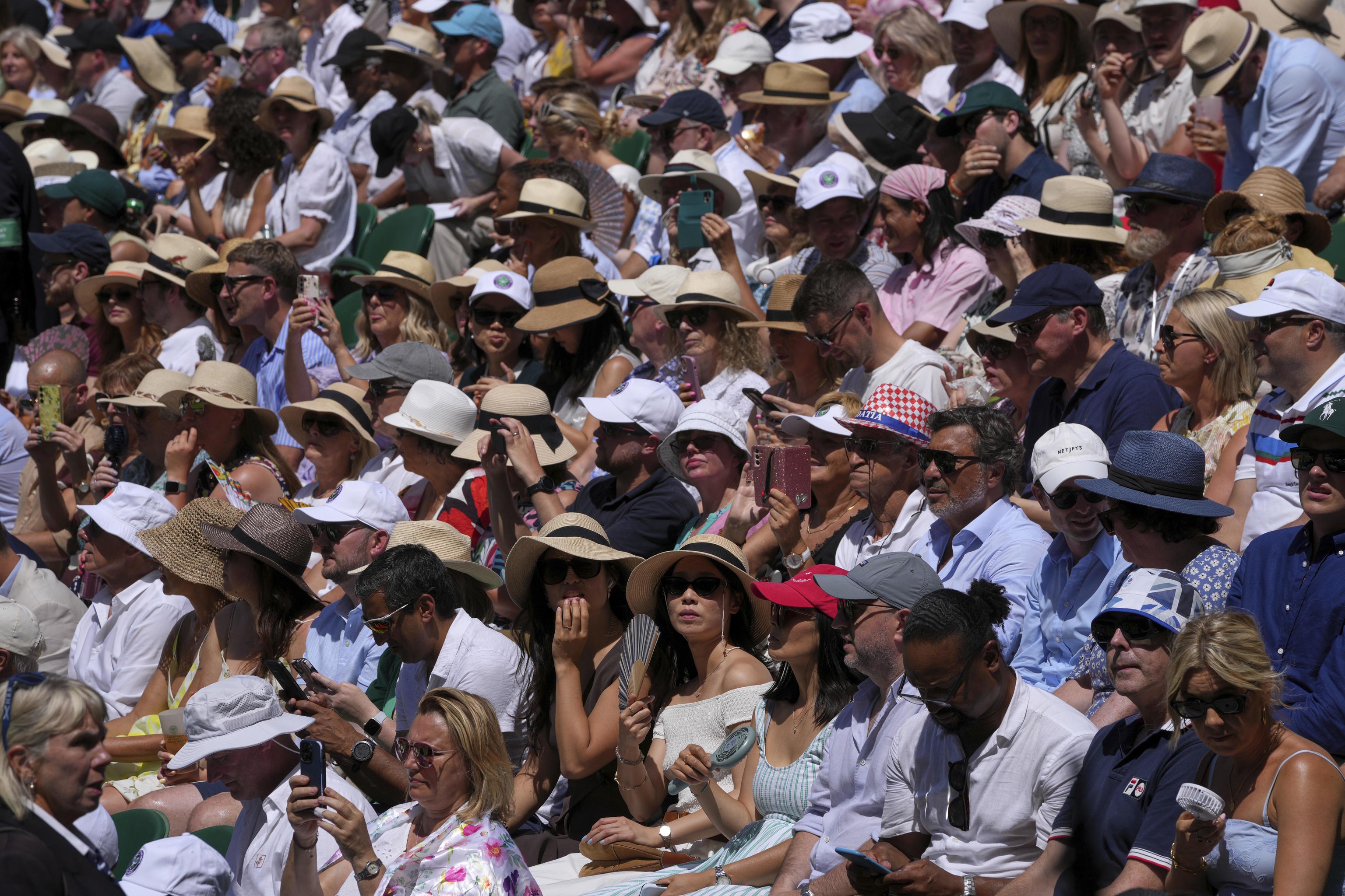 Spectators sit in the sun on Centre Court at the Wimbledon Tennis Championships.
