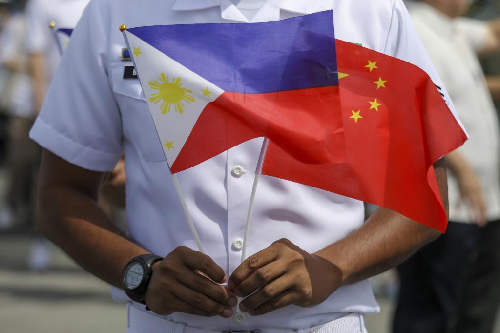 A member of the Philippine Coast Guard holds a Philippine and China flag.