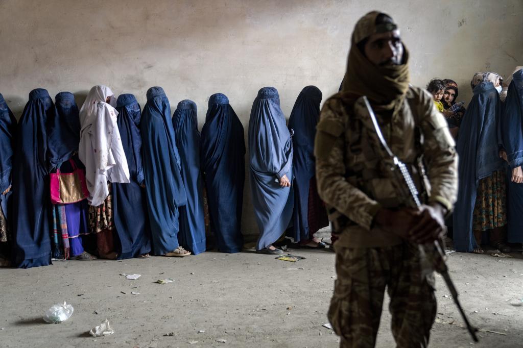 A Taliban fighter stands guard as women wait to receive food rations.