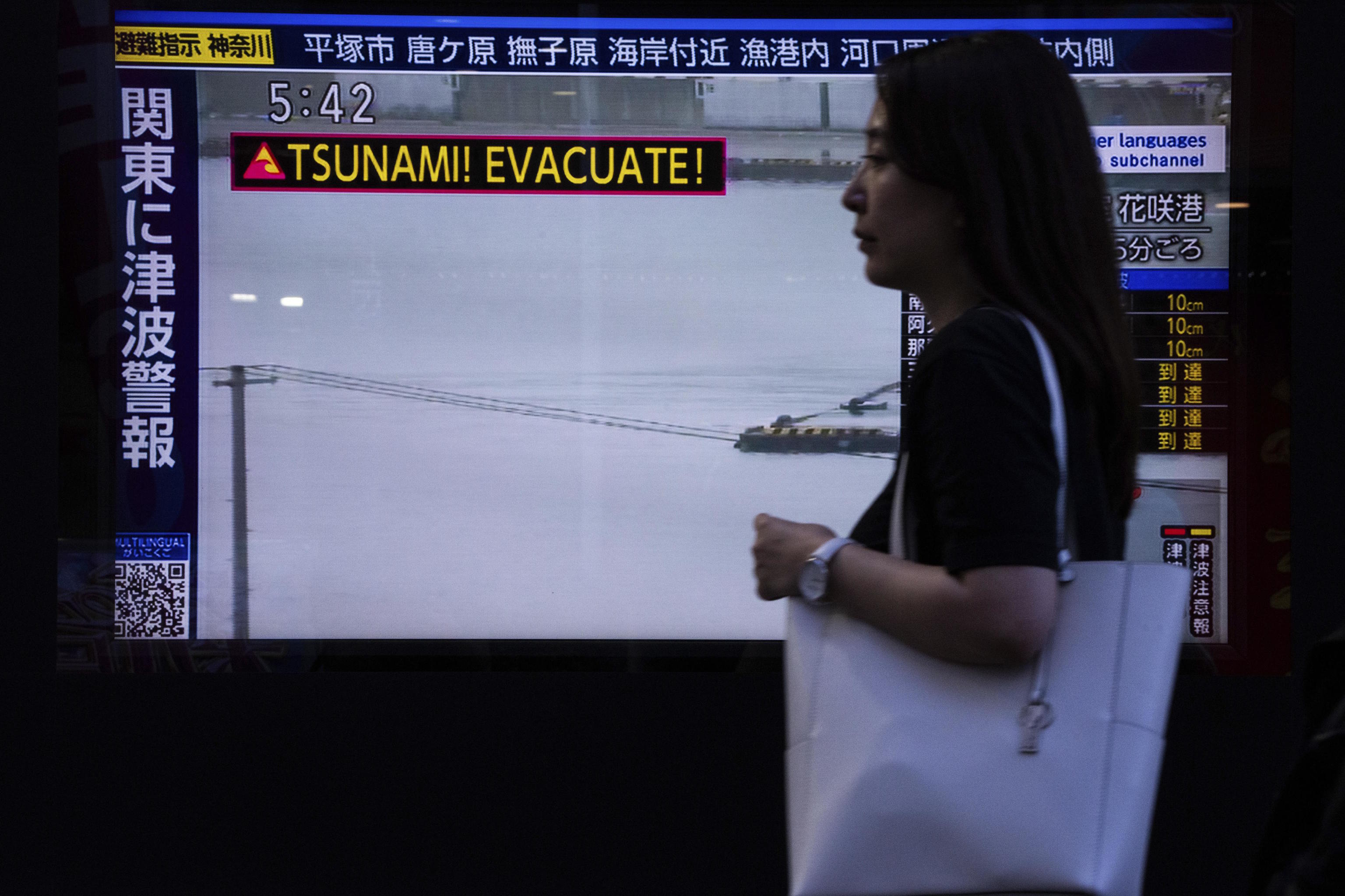 A pedestrian walks past a TV screen displaying a tsunami warning in Tokyo.