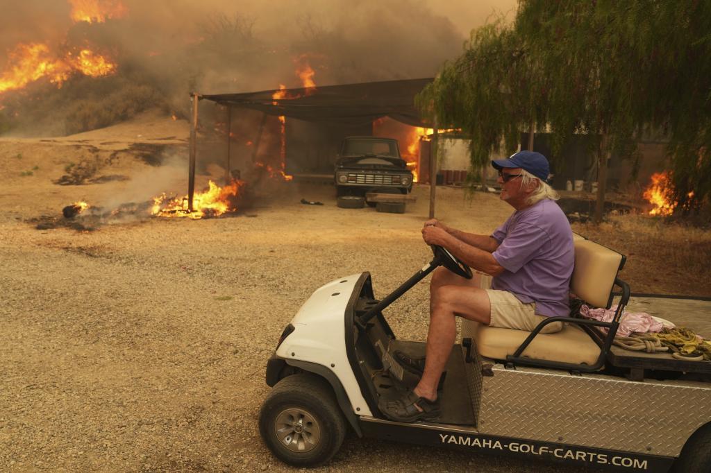 A resident rides a golf cart as he exits his property while the Canyon Fire