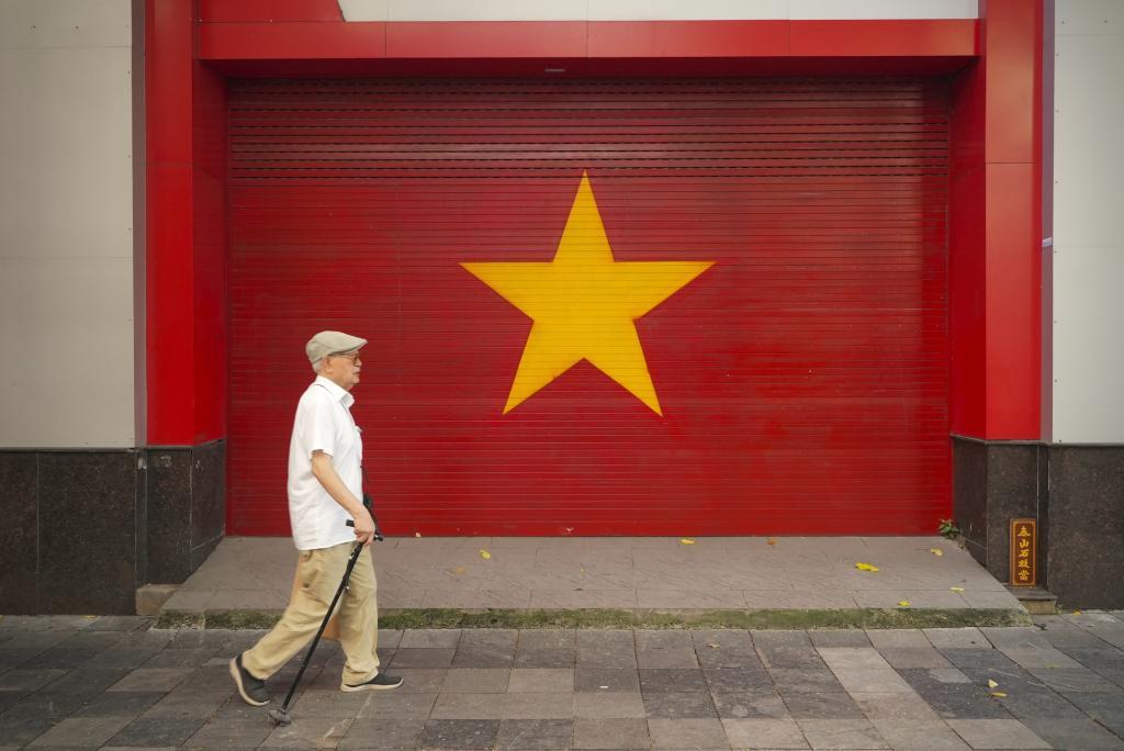A man walks past a Vietnamese flag painted on a wall in Hanoi