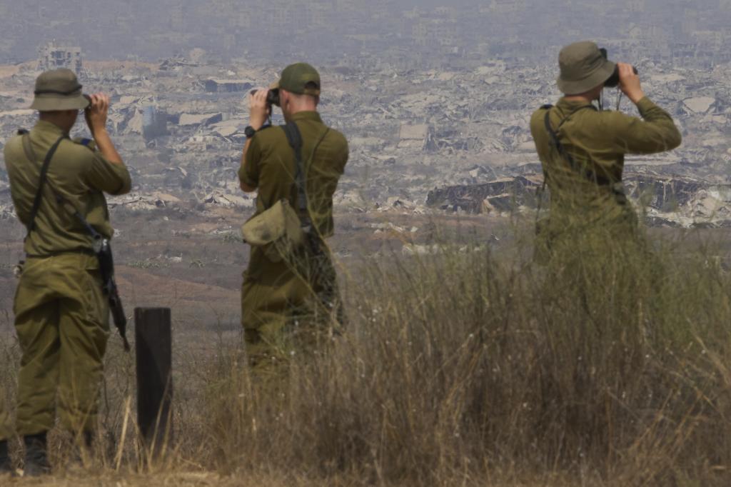 Israeli soldiers use binoculars to look at damaged buildings in the Gaza Strip from southern Israel,