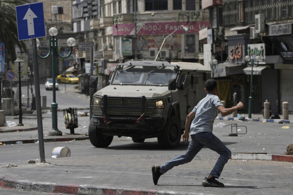 A Palestinian runs in front of an armored vehicle during clashes with Israeli forces