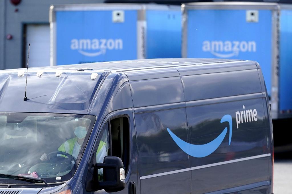 An Amazon Prime logo appears on the side of a delivery van as it departs an Amazon Warehouse location
