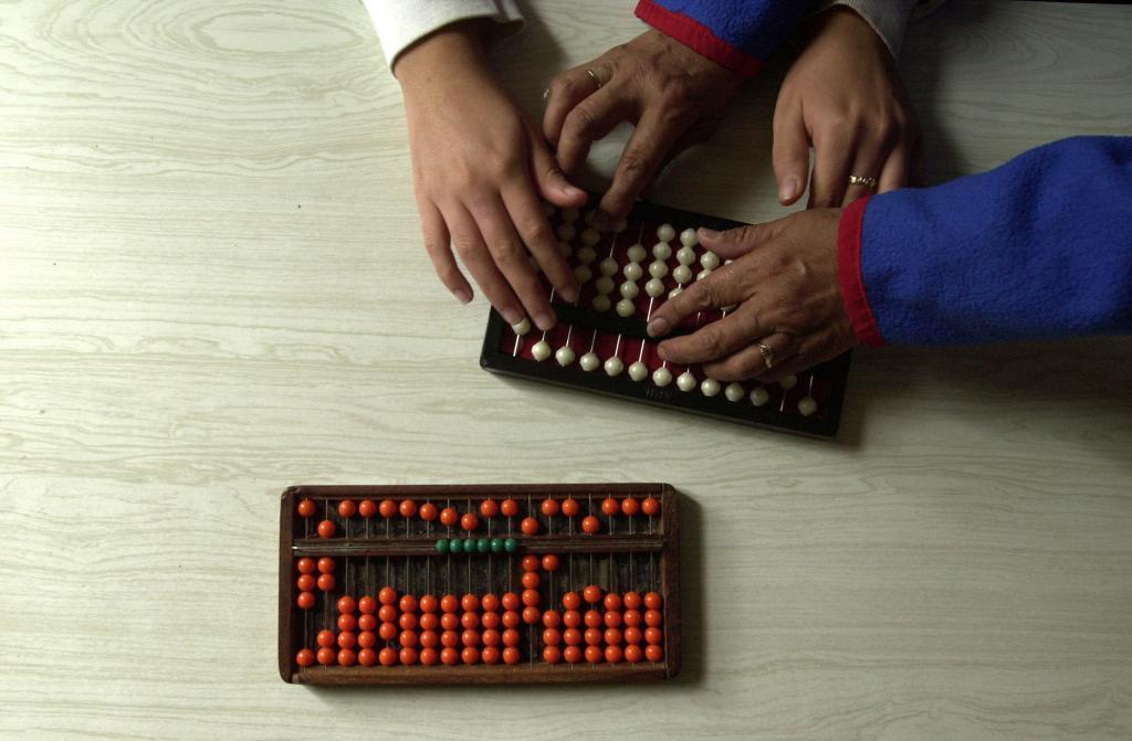 A teacher teaches a girl how to use the abacus during math class.