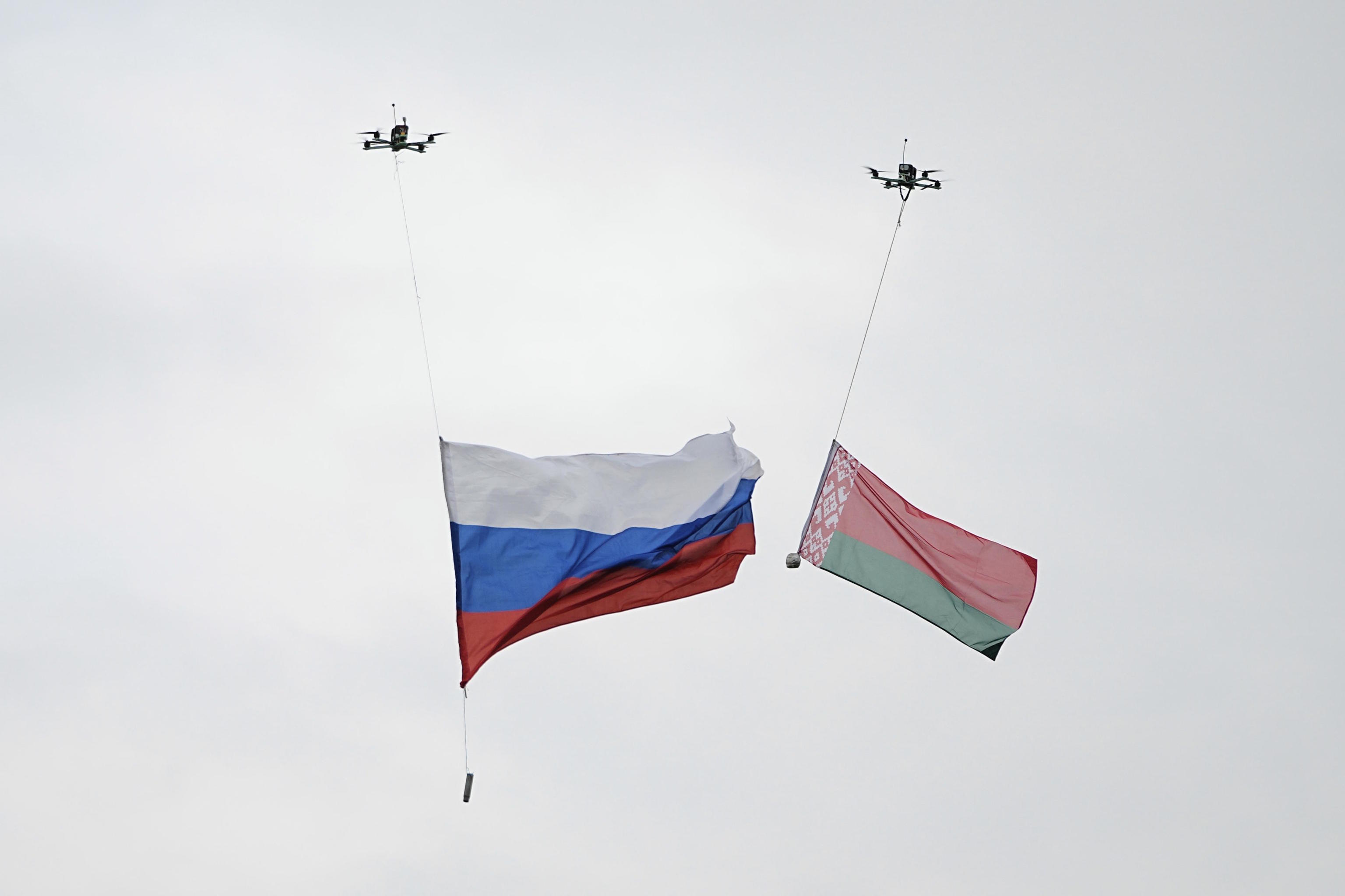 Drones each carry a Russia, and Belarus national flag at a training ground.
