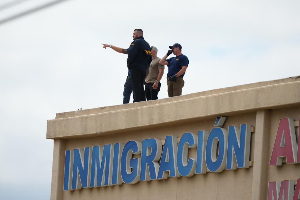 Law enforcement officers inspect the roof of an apartment building.