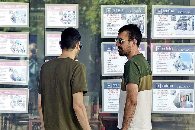 Two young people look at the window of a real estate agency.