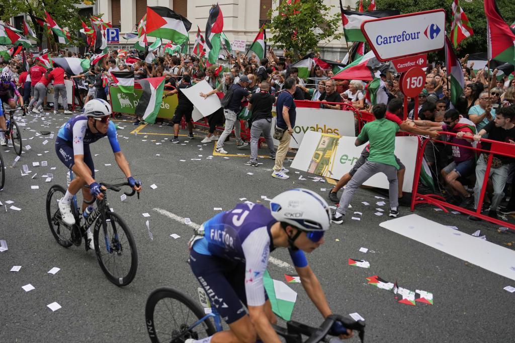 Israel Premier Tech cyclists compete while people hold Palestinian flags.