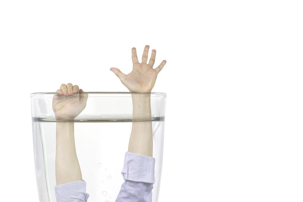 Image of a pair of arms showing from a glass of water representing the idea of drowning in a glass of water.