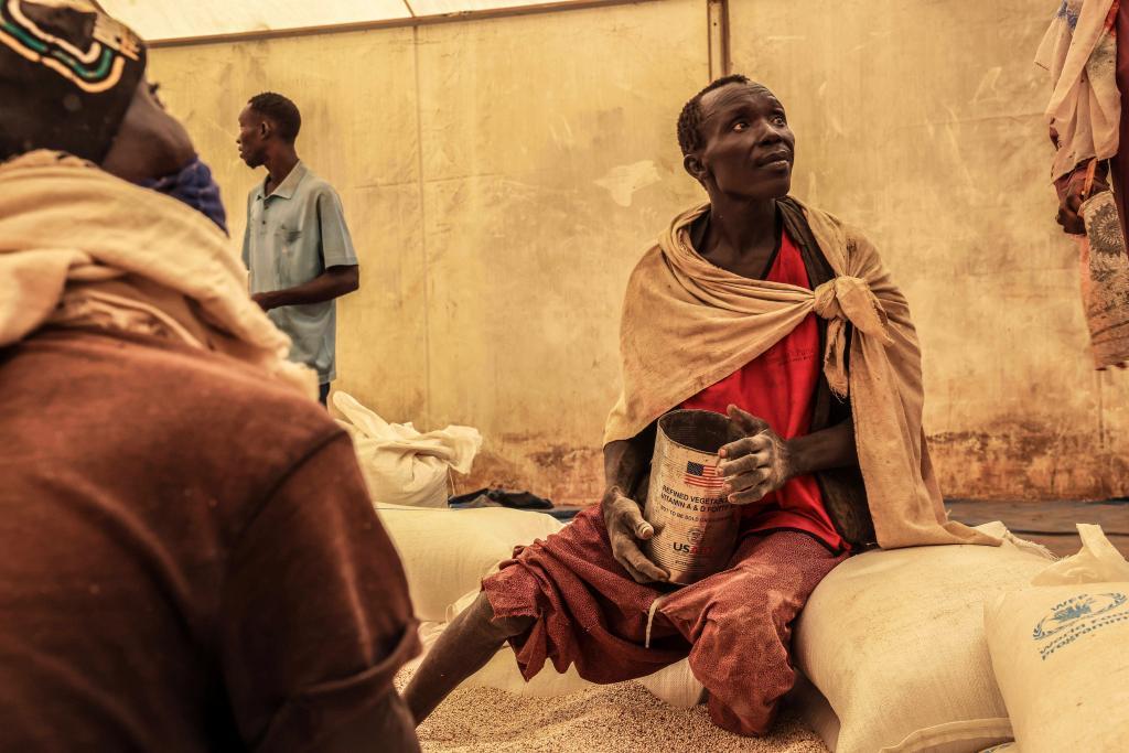 A man scoops up portions of wheat to be allocated to each waiting family after distribution by the U.N. World Food Programme