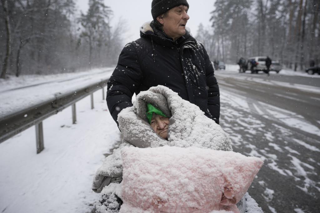 An elderly woman is coated in snow as she sits in a wheelchair after being evacuated from Irpin
