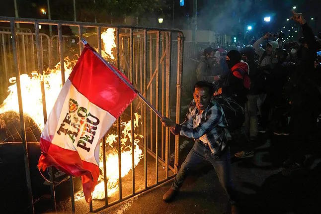A protester waves a Peruvian flag in front of the flames during a protest against the newly appointed interim president of the country, Jos Jer, in Lima.