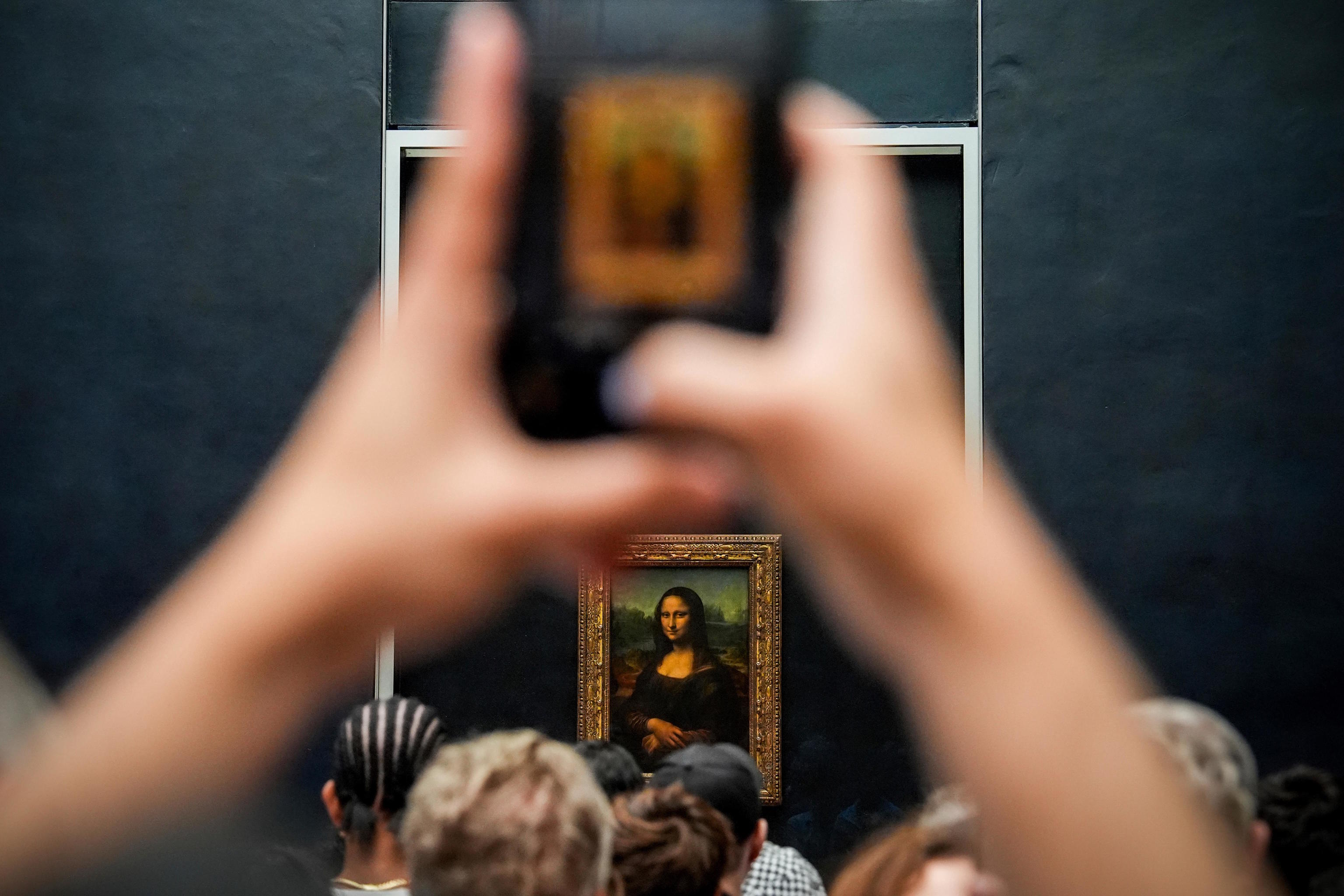 A person photographs Mona Lisa at the Louvre museum.