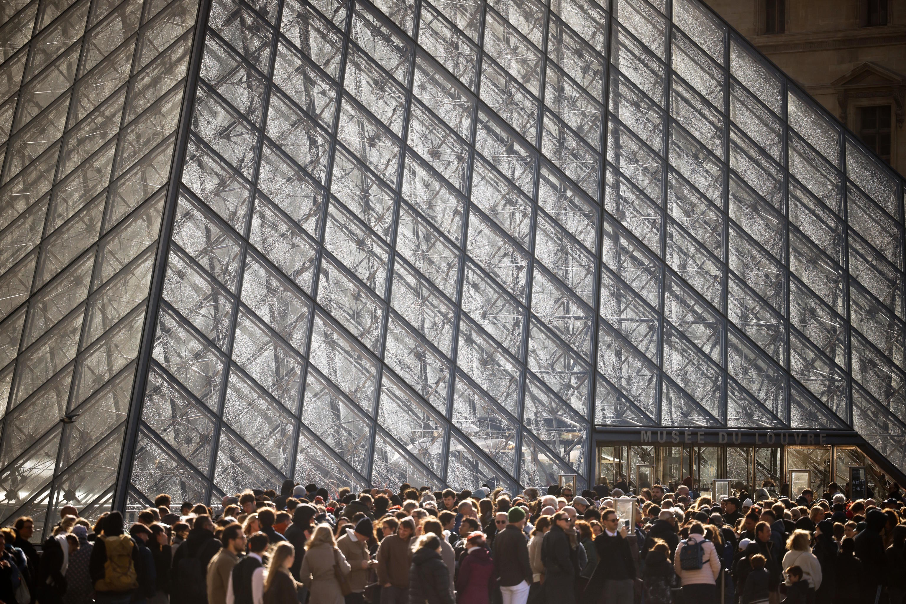 Visitors queue outside of the Louvre museum.