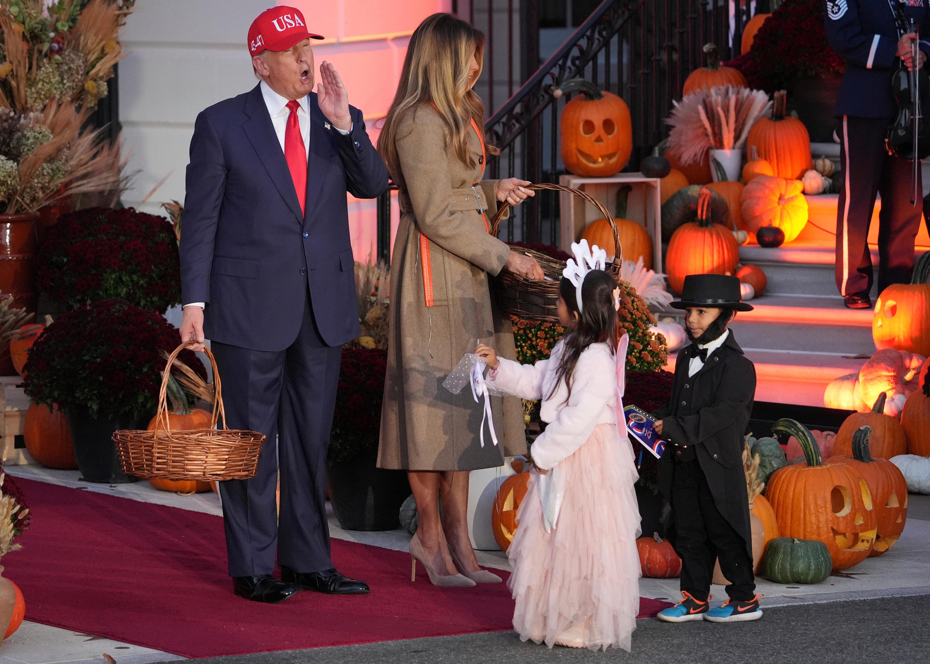 President Donald Trump and first lady Melania Trump hand candy to children dressed.