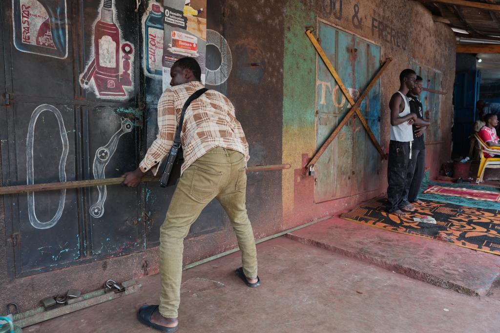 Oumar Bella Diallo, a returnee, opens the door of an auto repair shop where he works in Conakry