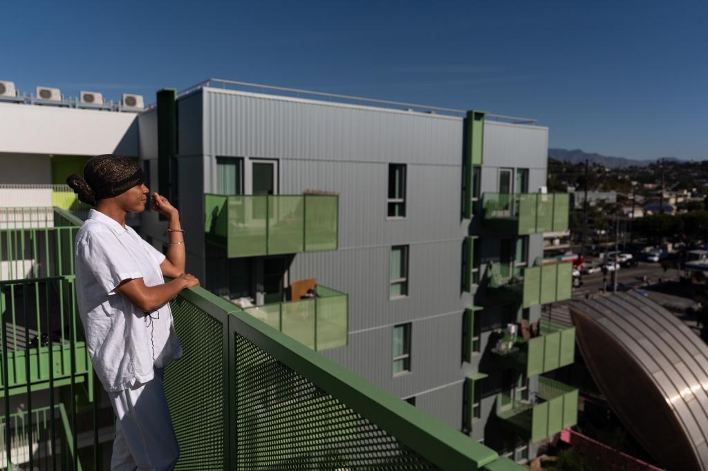 A woman pauses for a photo on the balcony of her studio apartment in the Santa Monica and Vermont Apartments in Los Angeles.