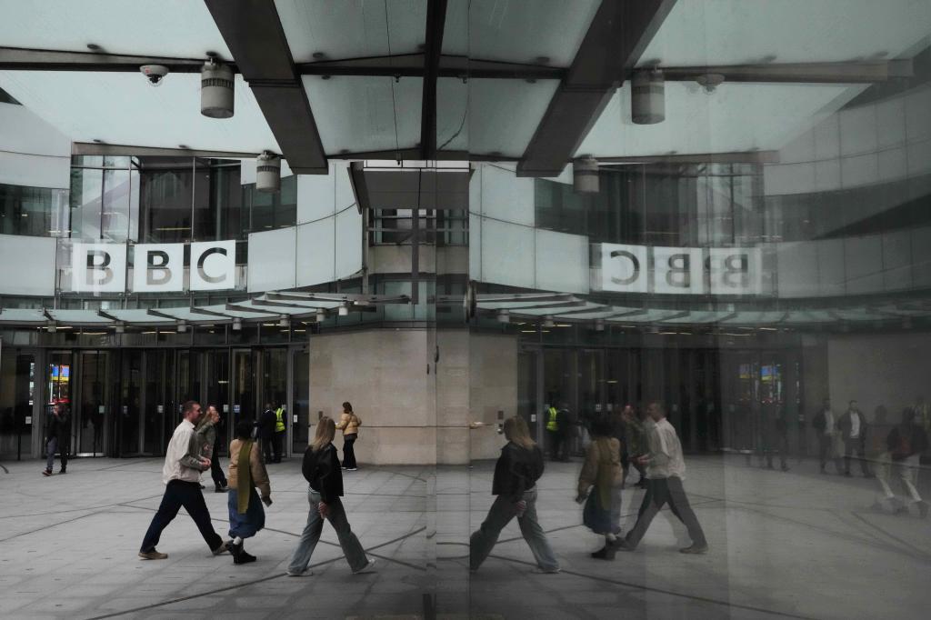 Pedestrians are reflected as they walk outside BBC Broadcasting House in London