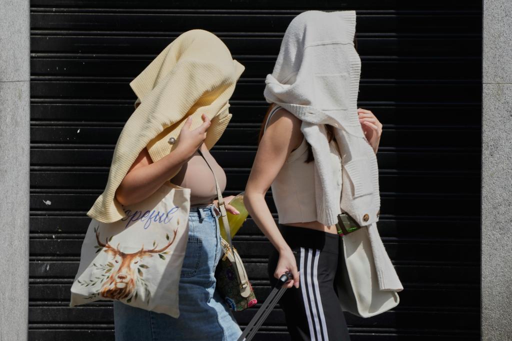 Two women walk with their heads covered to protect from the sun during extreme hot weather in Madrid.