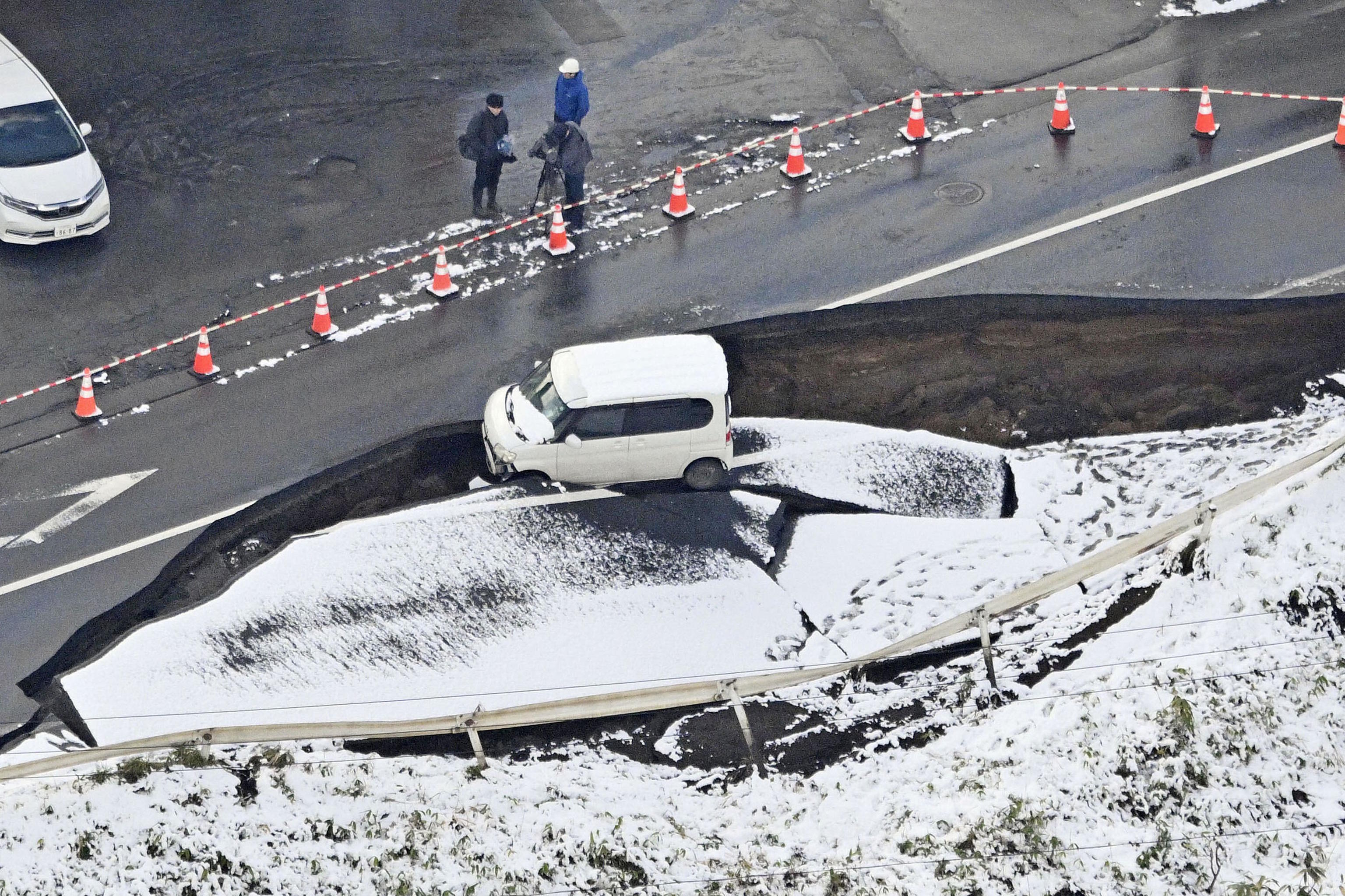 This aerial photo shows a vehicle sitting on a damaged road in Tohoku town.