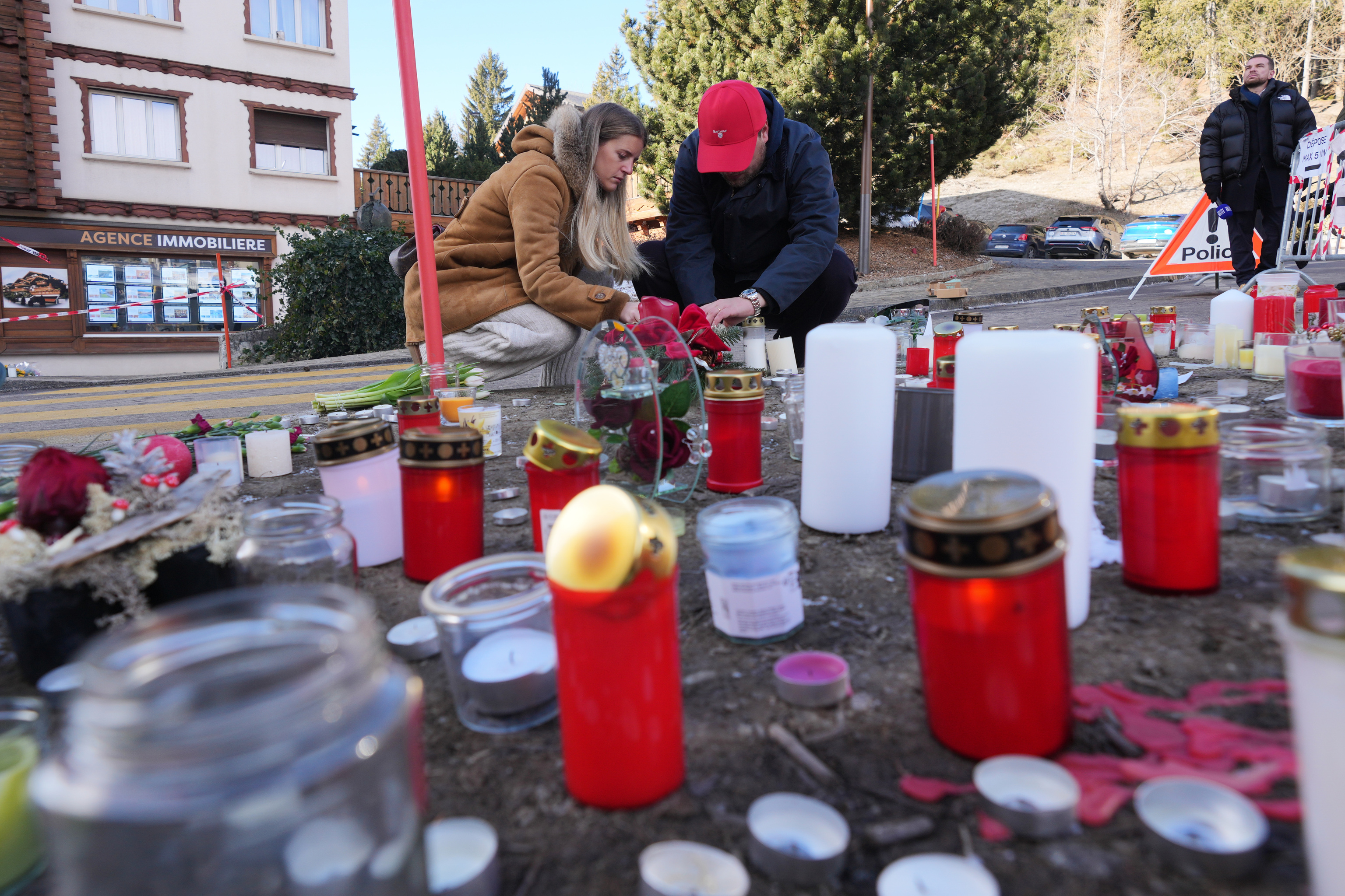 People bring flowers and candles near the sealed off Le Constellation bar, where a devastating fire left dead and injured during the New Year's celebrations.