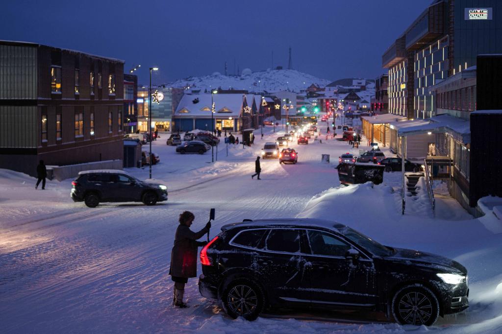 A woman cleans her car from snow in Nuuk.