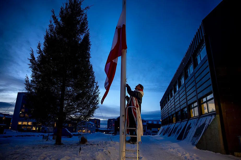 An official lowers the flag of Greenland in front of the Nuuk City Hall.