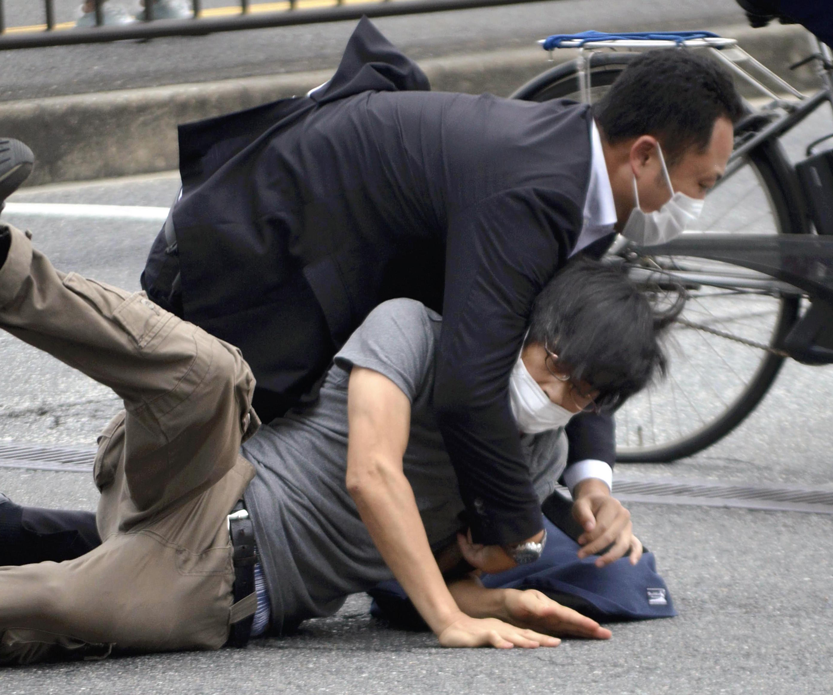 Tetsuya Yamagami, bottom, is detained near the site of gunshots in Nara Prefecture.
