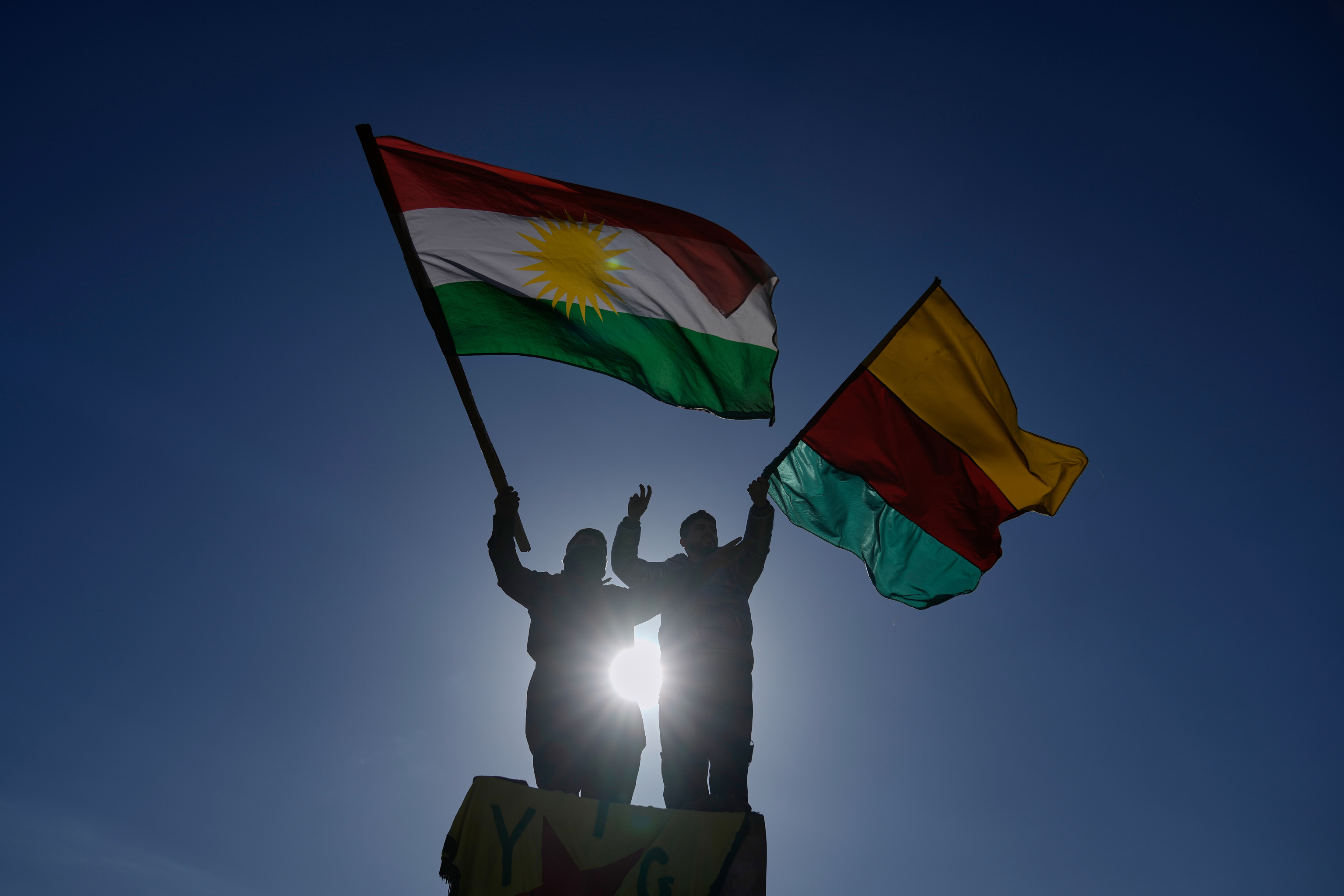 Protesters from the Kurdish community wave party flags.