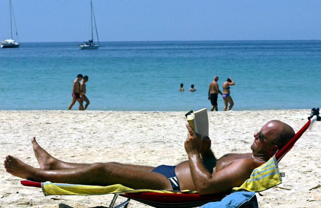 A western tourist reads a book as he enjoys sunbathing on Kata beach, in Phuket, southern Thailand