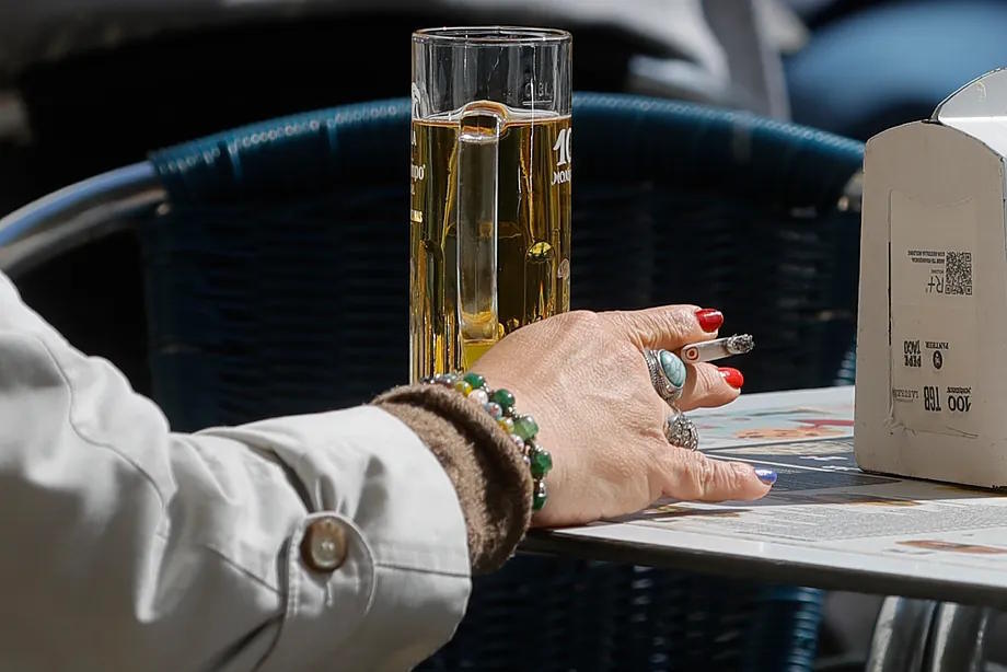 A woman on a terrace with a cigarette and a beer.